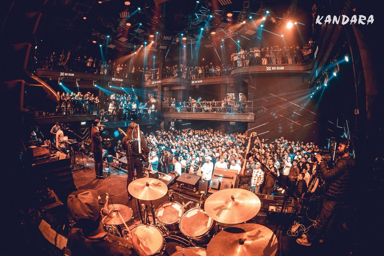 The band seen from behind the drum kit, hall packed to the back